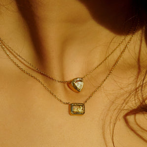 The Naipe Heart-ish Necklace featuring loose diamonds in a rounded triangle-shaped Kaleidoscope Shaker™. On close-cropped women's neck. Stacked above an emerald-shaped necklace with yellow diamonds. 