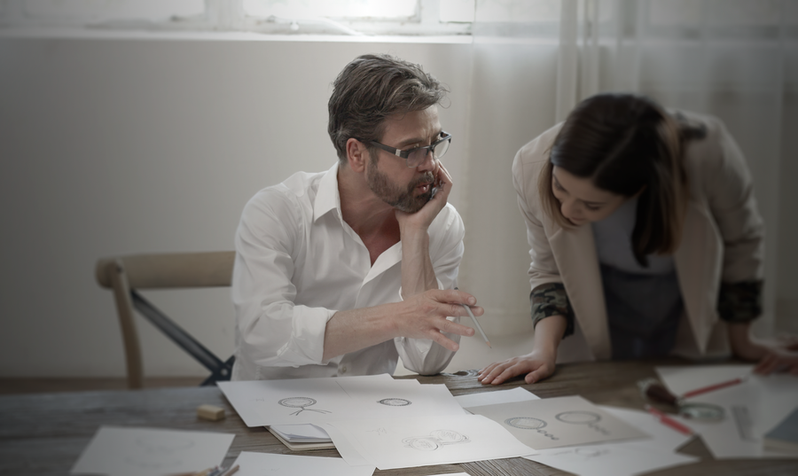 Moritz Glik sitting on a chair by a desk showing his drawing to a woman